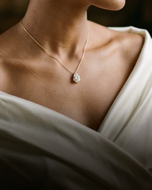 A pear-shaped diamond pendant on a fine gold chain resting below the collarbone